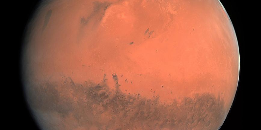 A view of Mars taken by the ESA Rosetta mission on its flyby past the planet. The deep orange red colour of its surface is broken by dark features on the surface and white polar ice caps at the top and bottom of the globe