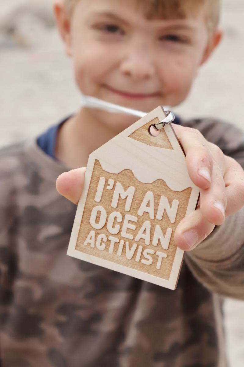 A boy holds up a wooden keyring with the words 'I'm an Ocean Activitist' on the front