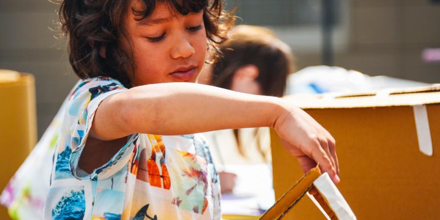 A young boy lifts the lid of a cardboard box during a craft activity at the National Maritime Museum