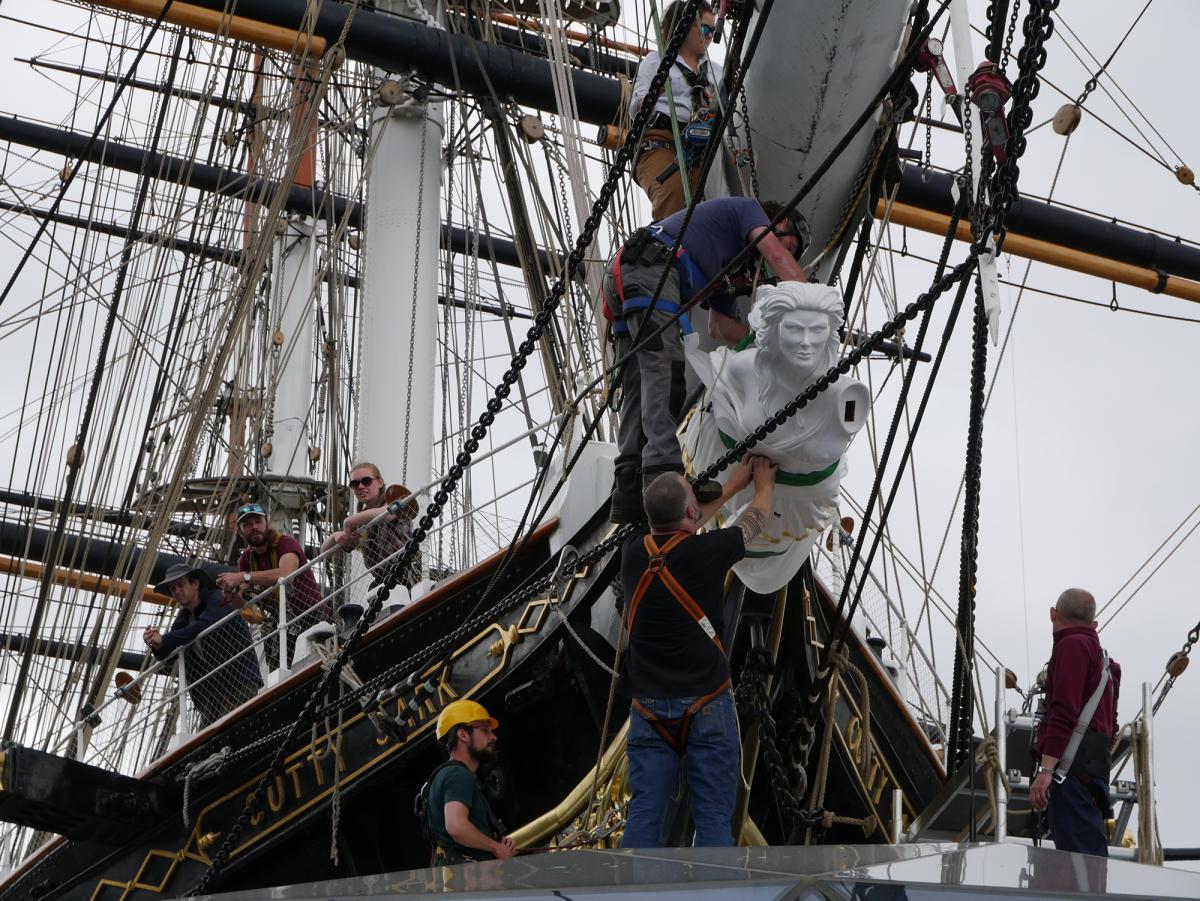 Shipkeepers wearing harnesses fit the new Cutty Sark figurehead on to the prow of the ship