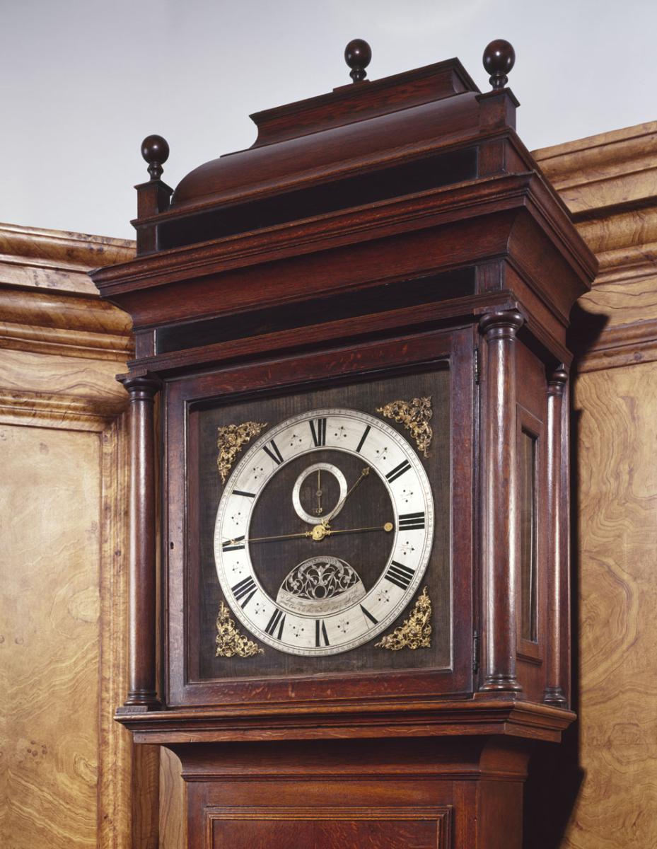 A pendulum clock housed in a dark wooden case, with a white dial and gold hands and decorations