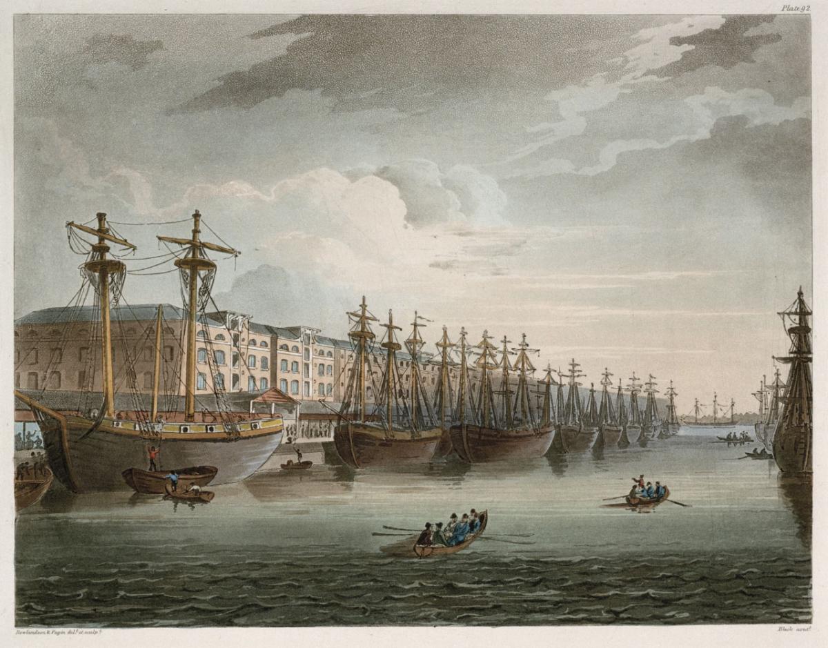 A detailed depiction of the West India Docks in 1810, showing large sailing ships moored next to warehouses on the left, and rowing boats in the centre of the frame