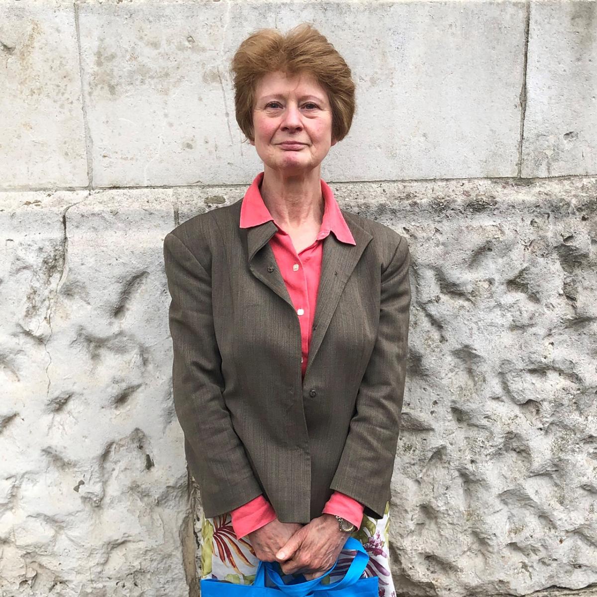 A woman looks directly at the camera. She is wearing a brown blazer and salmon pink shirt