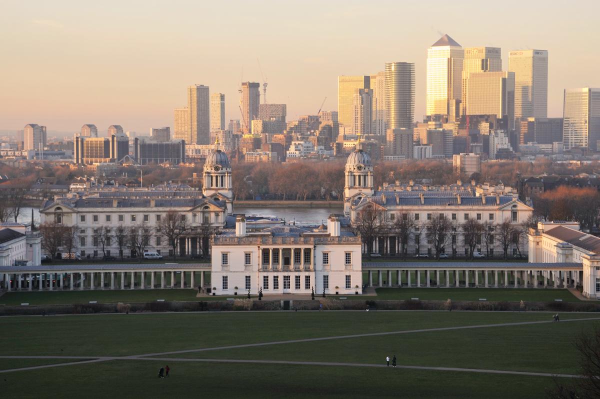 A landscape view taken from Greenwich Park, with the historic Queen's House and Old Royal Naval College in the foreground and the rising towers of Canary Wharf behind