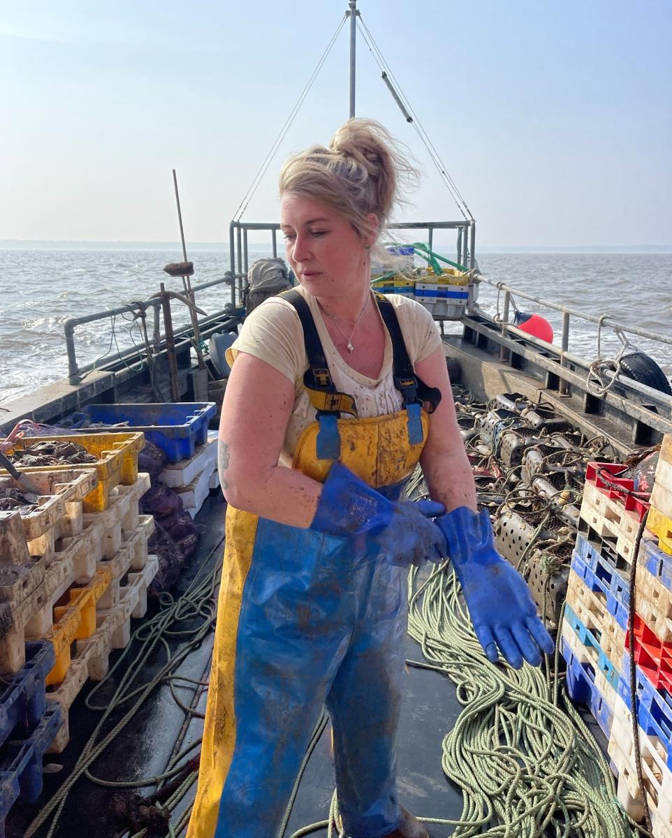 Ashley Mullenger in a boiler suit working on fishing boat surrounded by crates