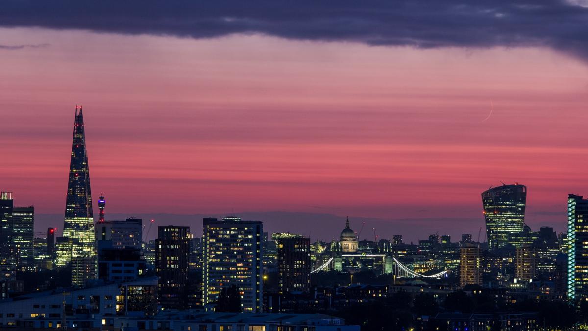 Image of London at dusk with a pink sky and a very thin crescent moon visible