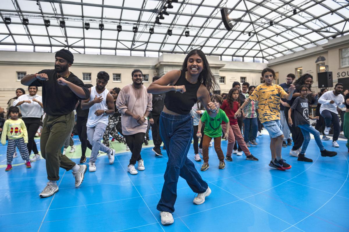 The image shows a woman dancing with a number of children and adults behind her copying her dance moves.