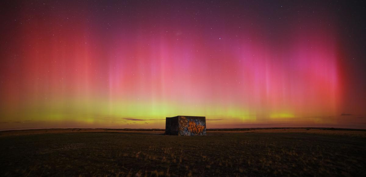 Image of a square building with graffiti on it, but in the sky is pink aurorae covering up to 50% of the image, which becomes yellow towards the horizon