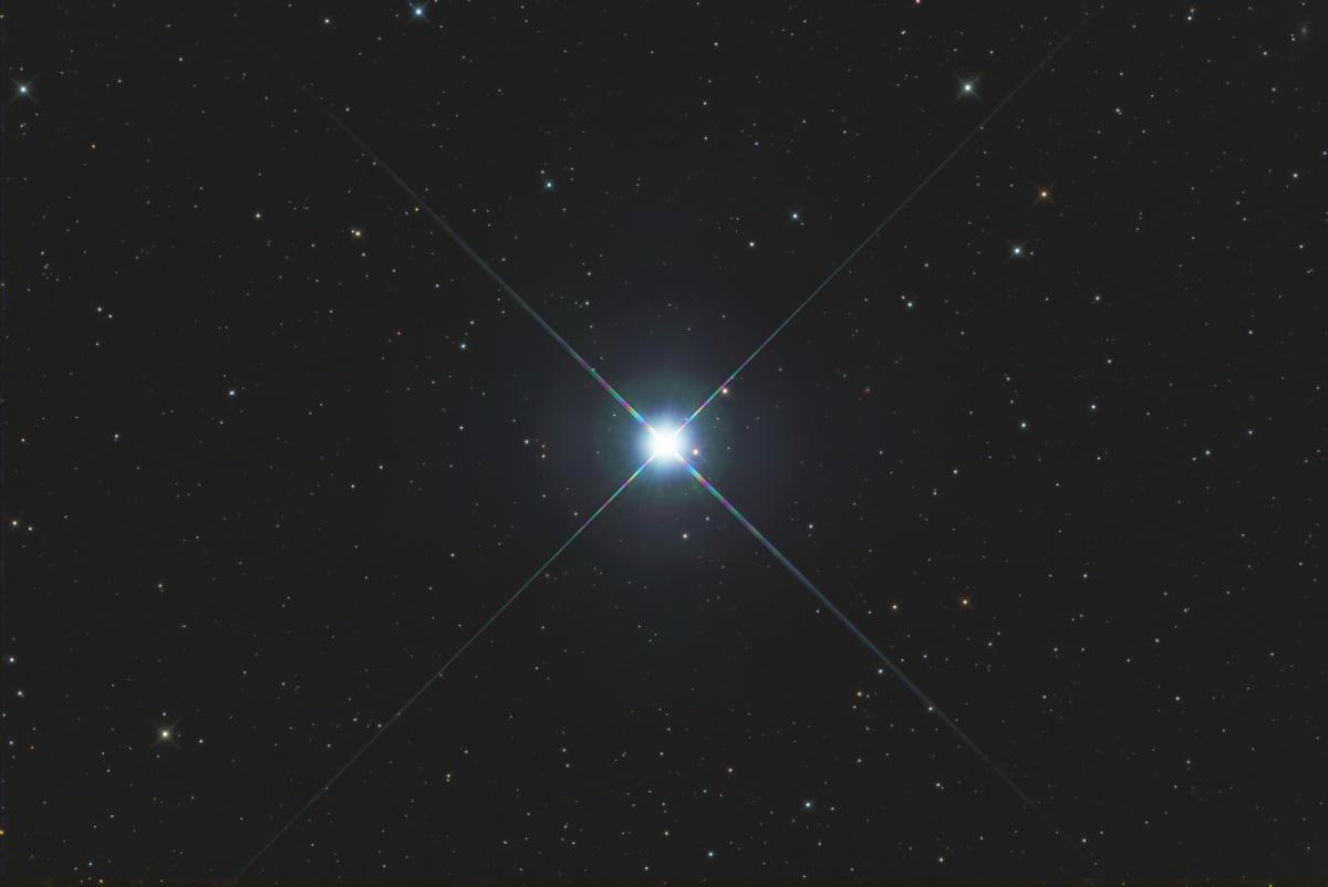 Image of a black starry night sky, with one very bright white and blue star in the centre with reflective lines coming off of it