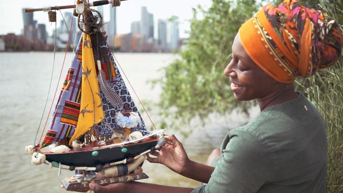 Image of a woman next to the Thames, holding a model boat