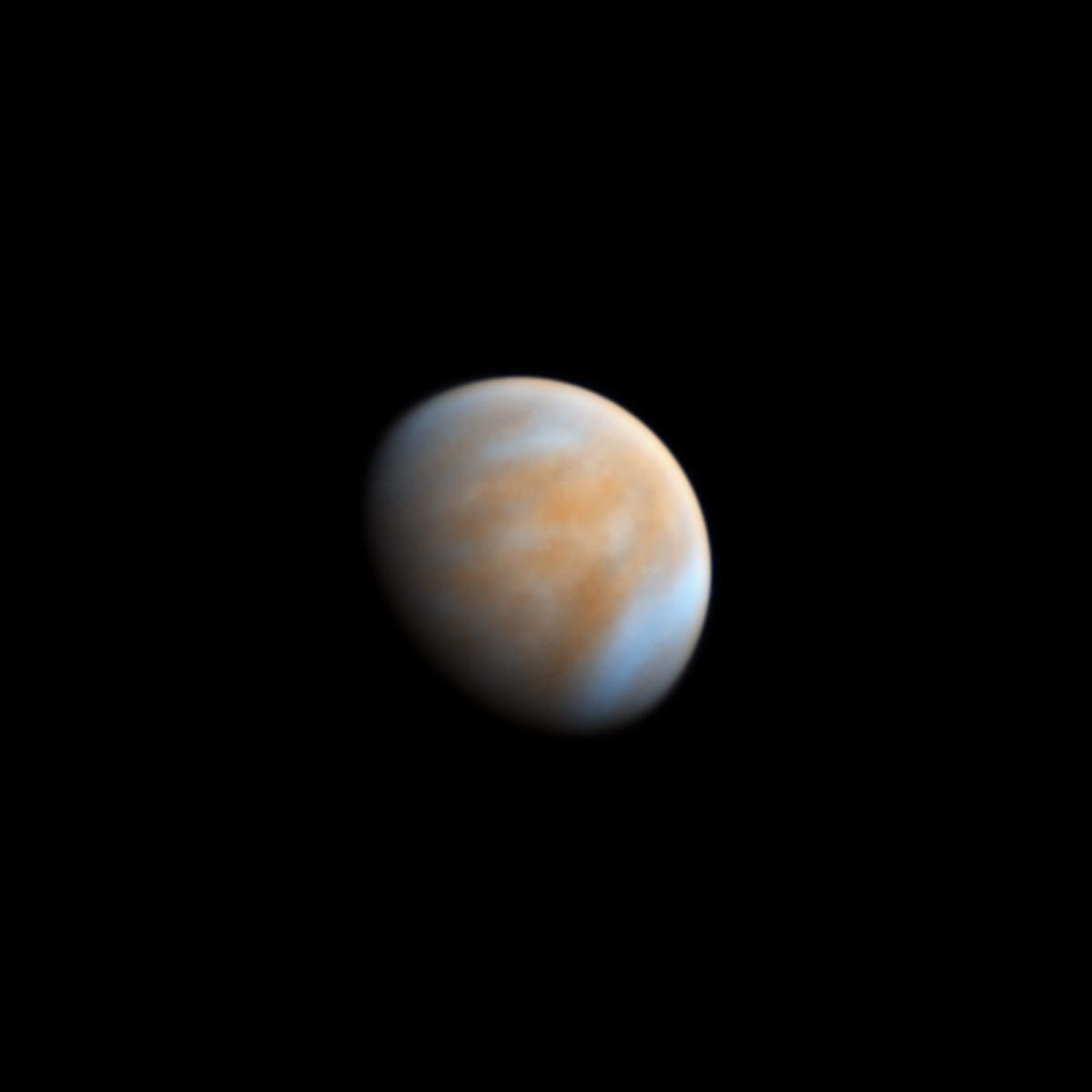 A telescope of view of Venus, shown in part shadow, appearing as a hazy orange and creamy white globe in a pitch black sky