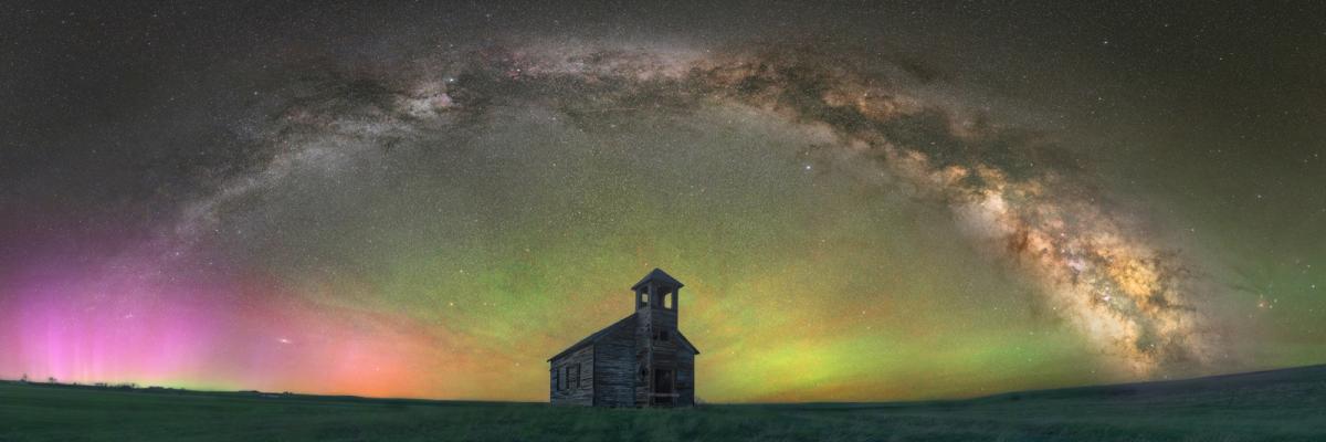 Abandoned church underneath pink and green aurorae and Milky Way