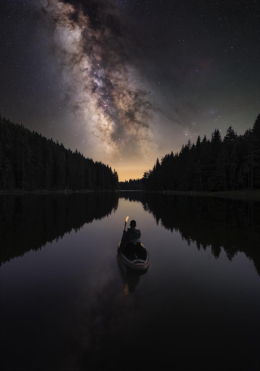 Silhouette of a person in a kayak on a lake with Milky Way stretching above