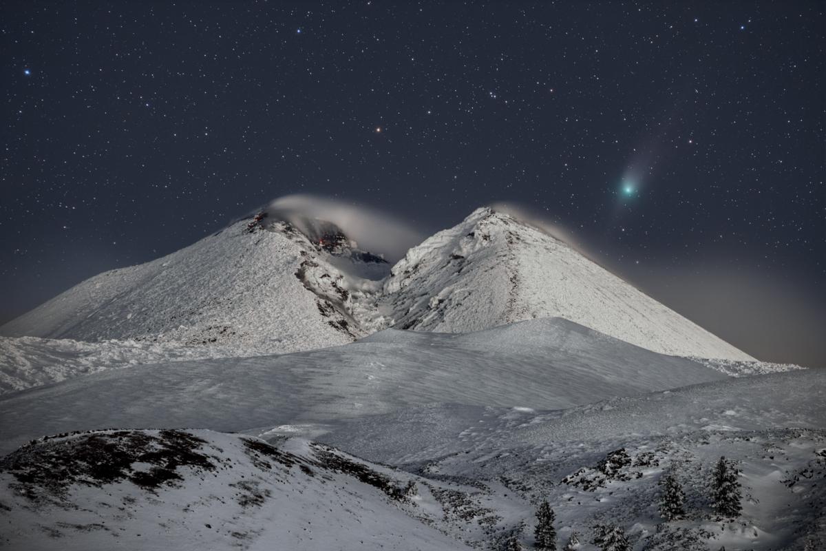 Image of a snowy mountain with a sark sky in the background. Comet C/2022 E3 (ZTF) is visible as a green smudge on the right hand side of the sky