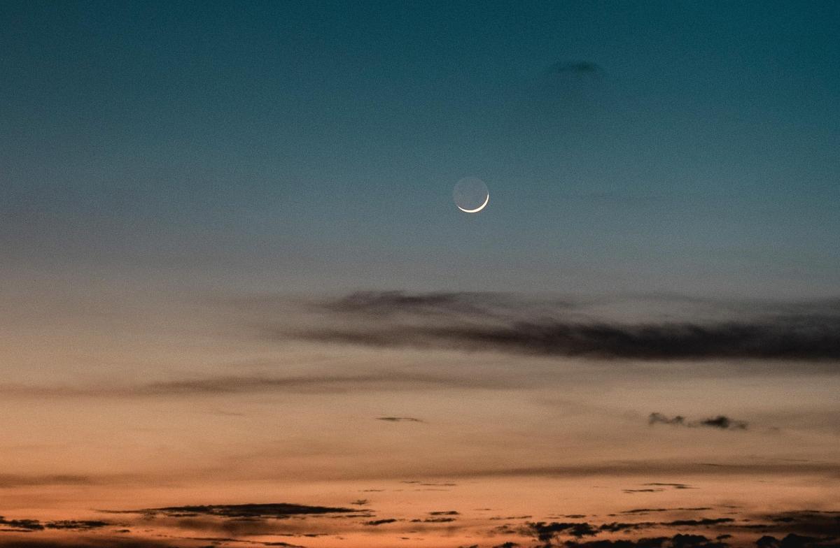 Image of new crescent Moon against the sky with sunset and black clouds