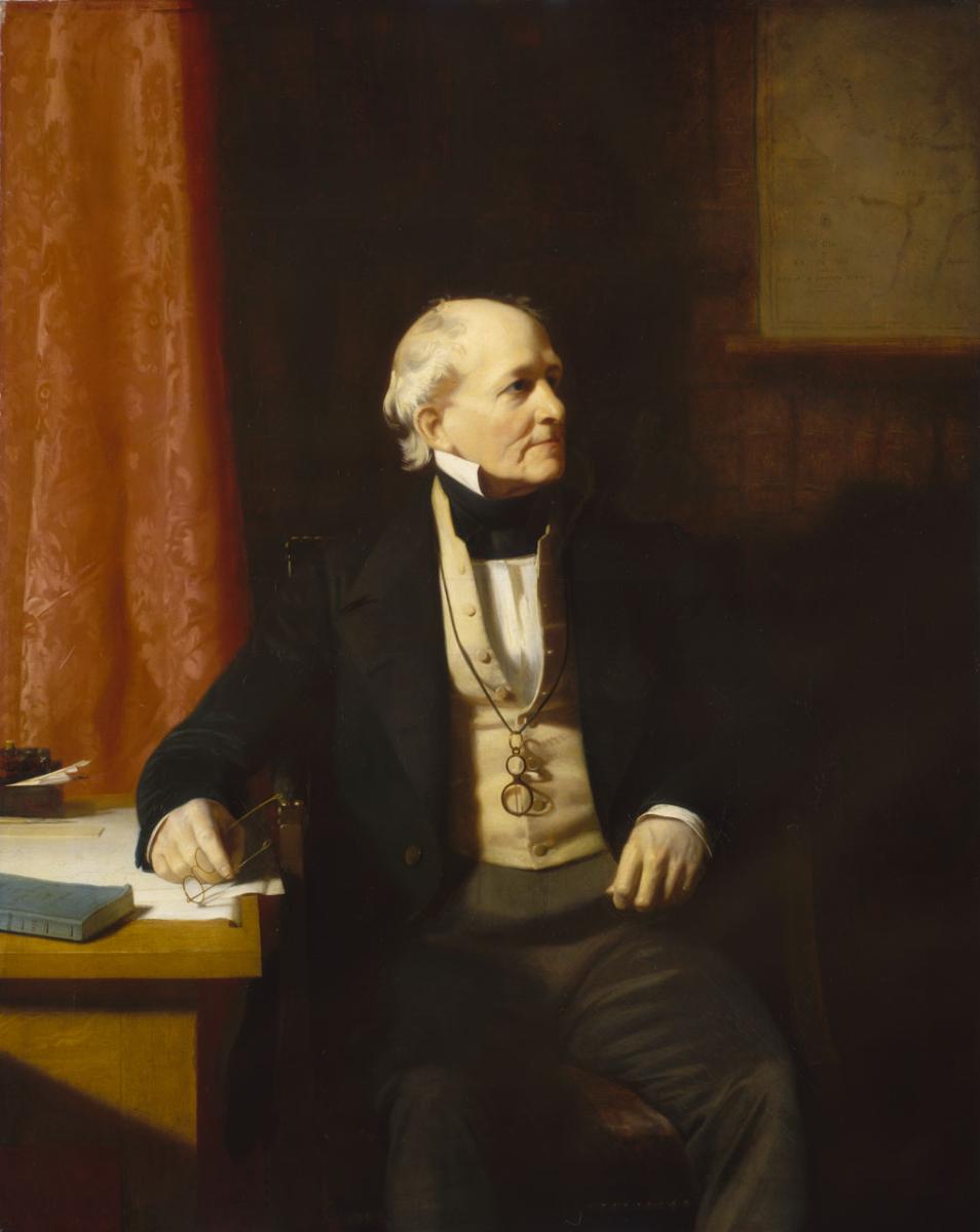 Portrait of a man wearing dark clothes and sitting in an armchair by a desk