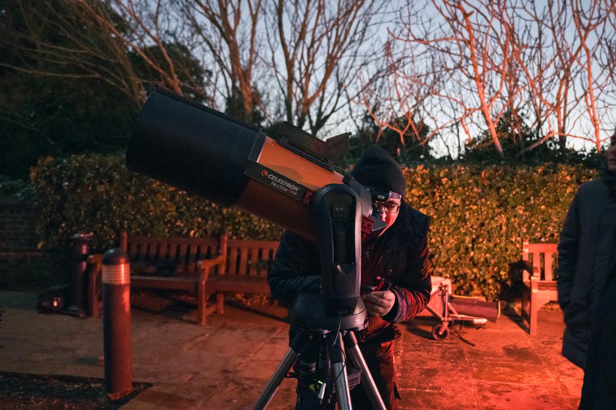 A man leans in to a telescope eyepiece during an evening astronomy event