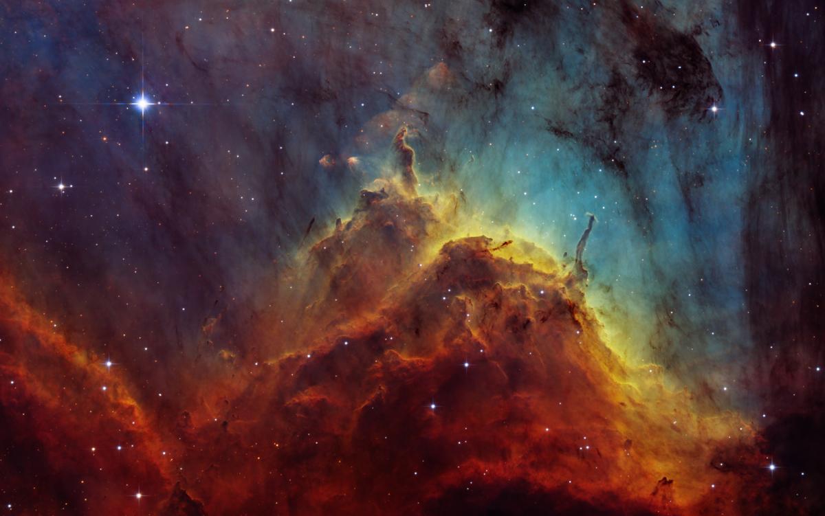 Image of a nebula, clouds of gas and dust in space, in a mountain range formation, the mountains are shades of red and yellow and behind are blues and blacks