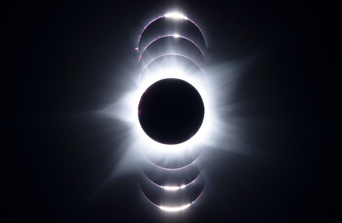 Image of a solar eclipse at the moment of totality, a dark black circle with streams coming off of it. Above and underneath are semicircles of light with light patches which show parts of the Sun shining out from behind the Moon