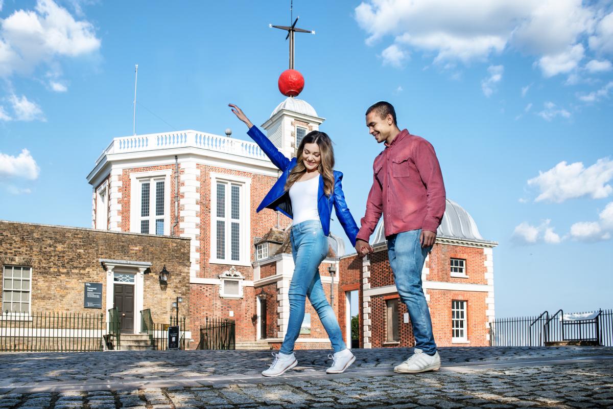 A woman and a man walk hand in hand along the Prime Meridian Line at Royal Observatory Greenwich