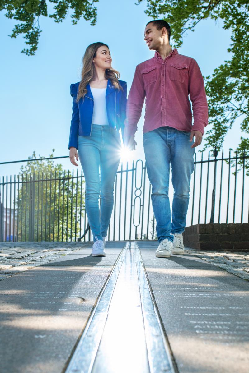 A couple holds hands as they walk either side of the Prime Meridian line at Royal Observatory Greenwich