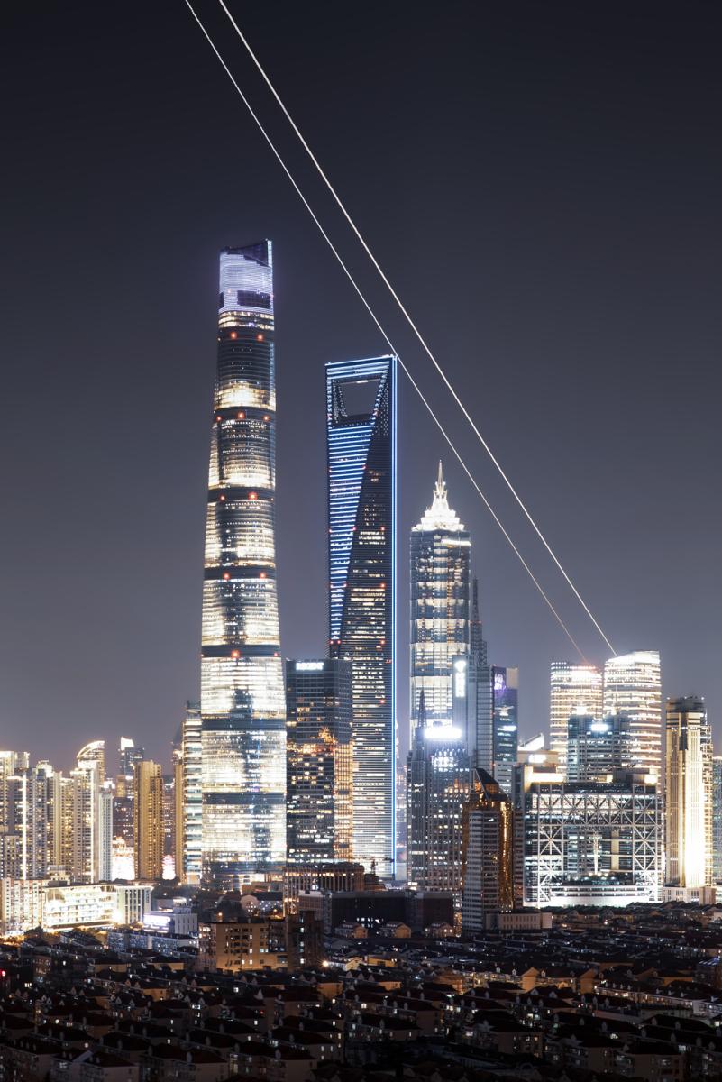 Image showing a cityscape with very bright skyscrapers lit up with bright golden and yellow lights at night, the sky behind is also bright from the glow, but there are two clear lines running parallel to one another moving diagonally from the top of the image to behind the buildings