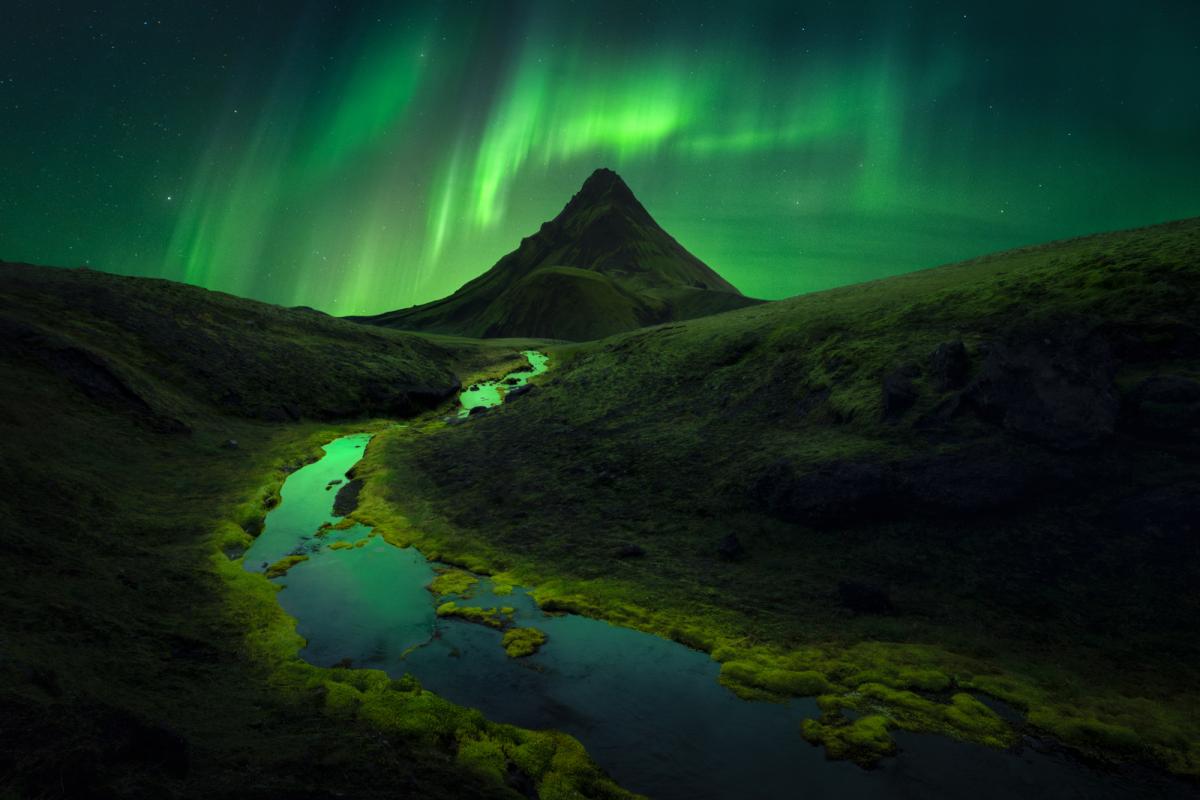 Green aurorae over a mountain and a winding stream in Iceland