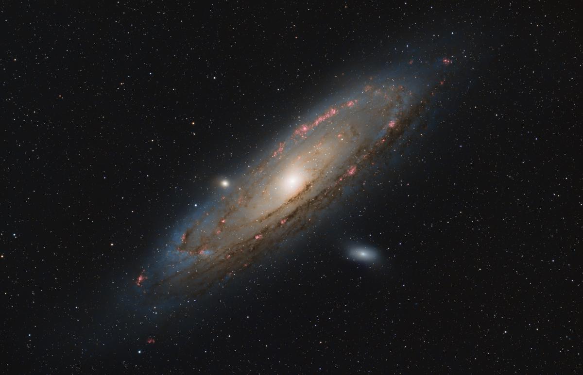 Telescope view of the Andromeda Galaxy, showing a diagonal spiral of stars against a dark black background 