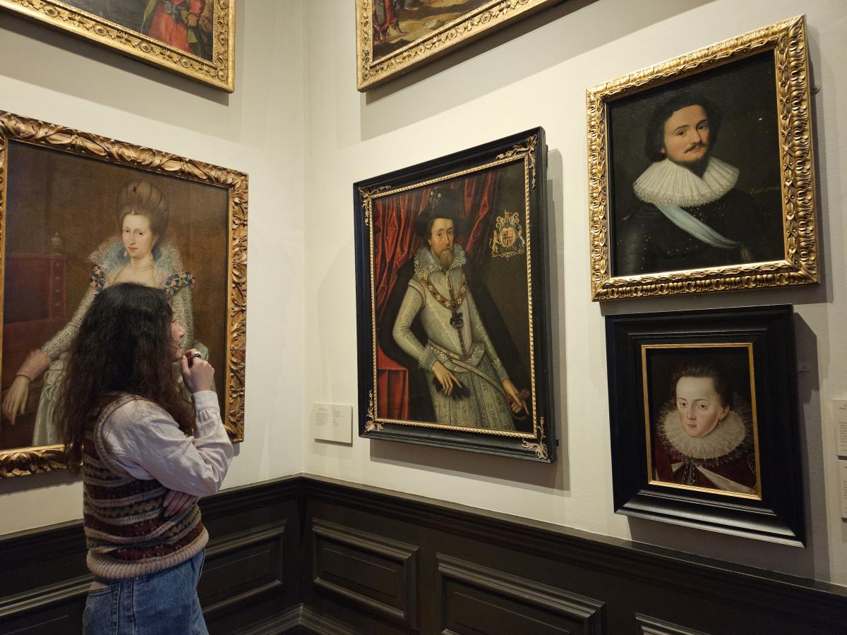 A woman gazes at portraits of historic figures. Three paintings are displayed in a gallery in front of her