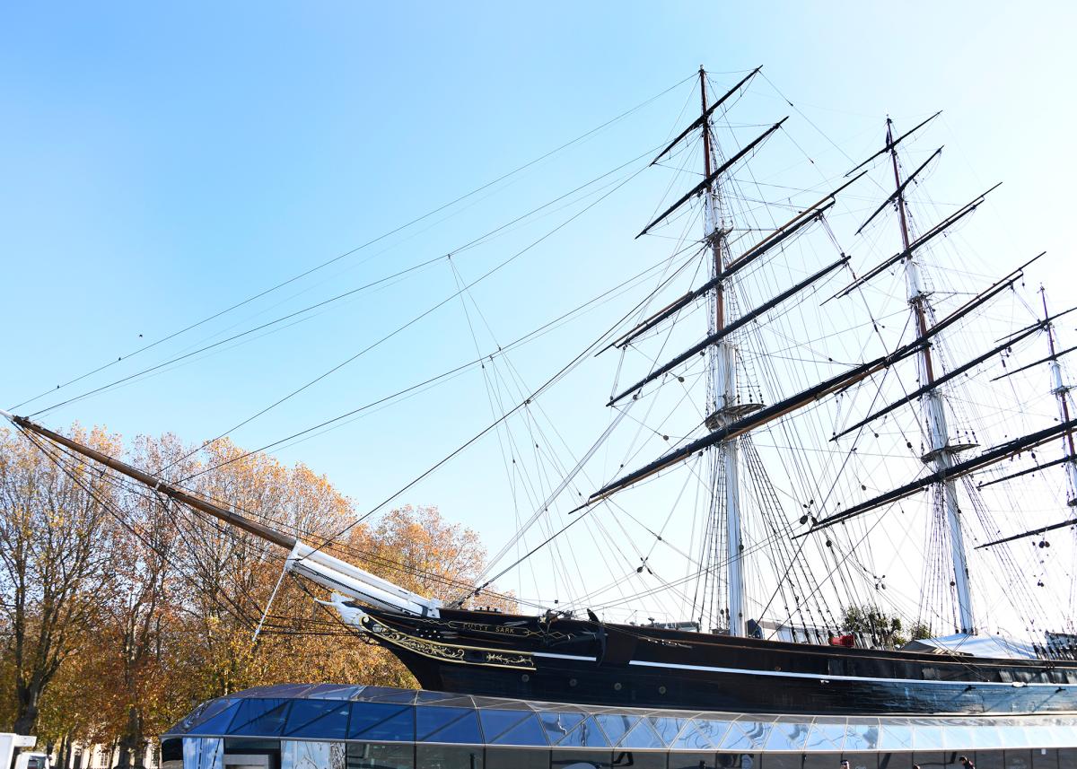 Exterior view of Cutty Sark in the sun. The masts of the ship are silhouetted against a bright blue sky