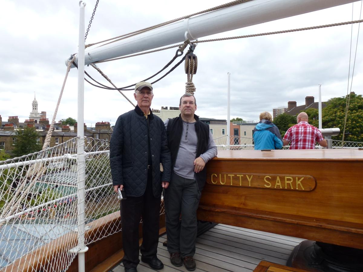 Two men stand side by side at the stern of historic ship Cutty Sark. The ship's name is visible in the lower right.