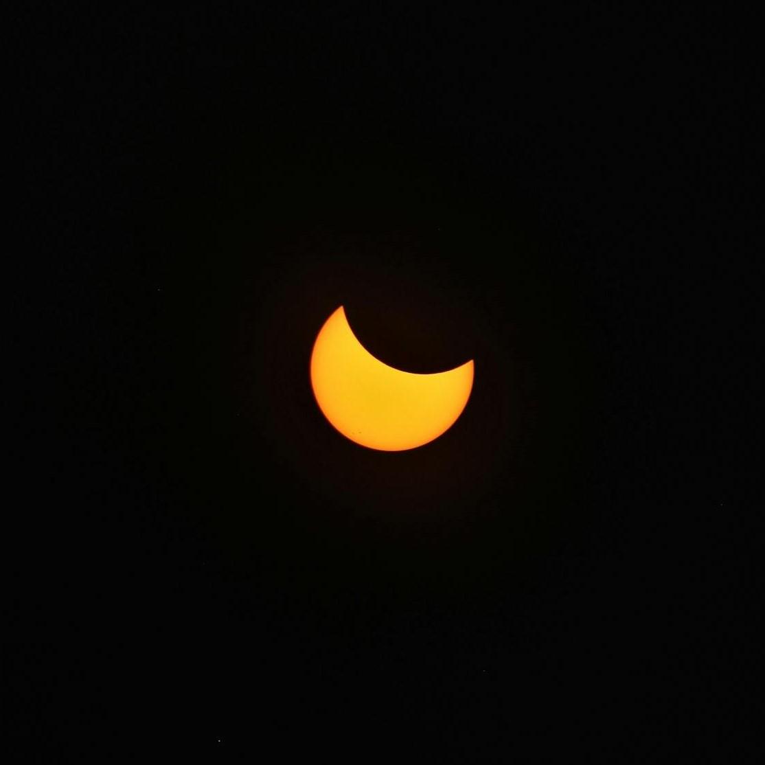 Thick yellow crescent of the Sun with a circular section missing in the top right corner against a black background