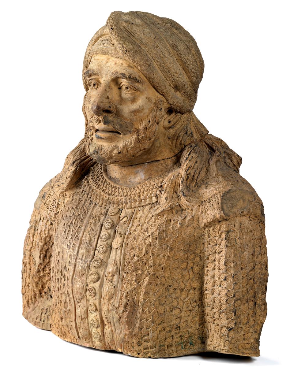 Cream-coloured terracotta bust said to depict a Moroccan man. He wears a headscarf and a patterned tunic