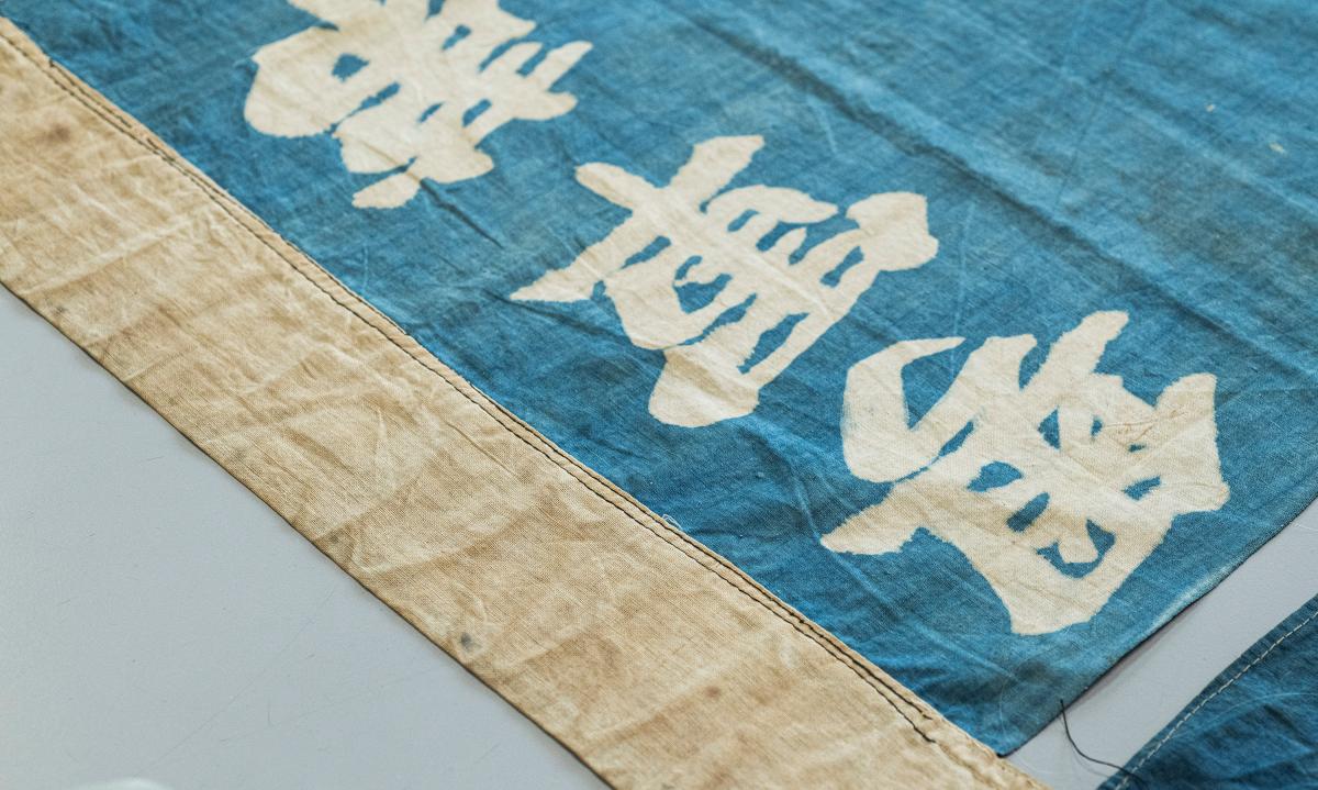 The edge of a blue ship's flag, with white Chinese characters visible, laid out on a table