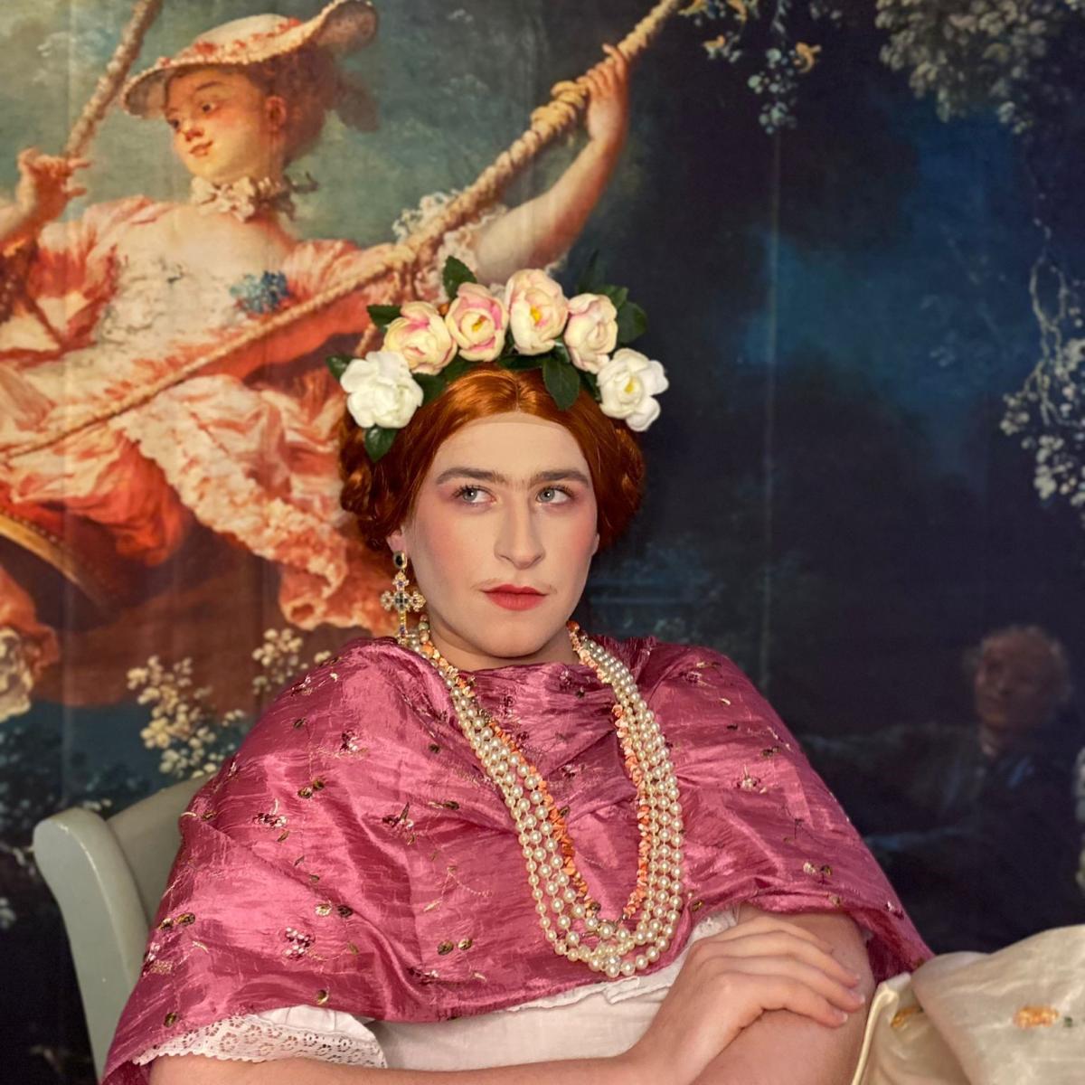 A woman lounges in a velvet pink dress, necklace and flower headpice