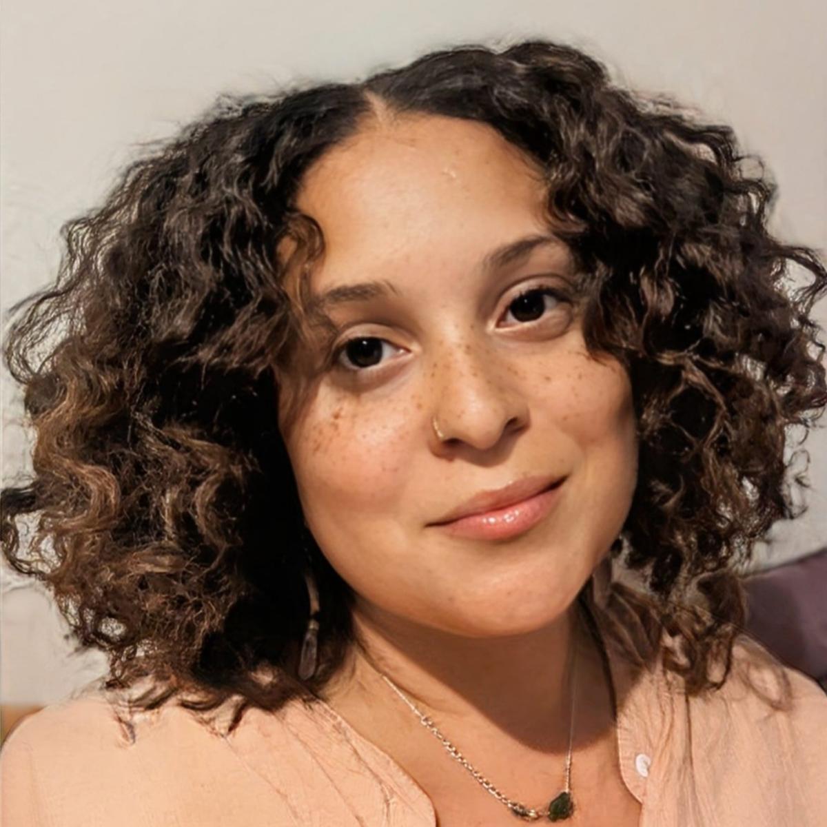 Colour photo head shot of a mixed heritage woman with curly shoulder length hair