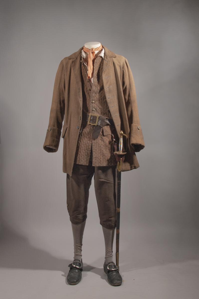 Original costume for Will Turner from Pirates of the Caribbean: The Curse of the Black Pearl. The costume includes a brown cotton jacket, waistcoast and breeches. A sword hangs from a leather belt around the waist 