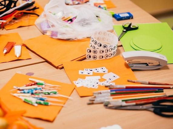 Photo showing crafting materials including bright coloured card, googly eyes stickers and pens, paint and paintbrushes