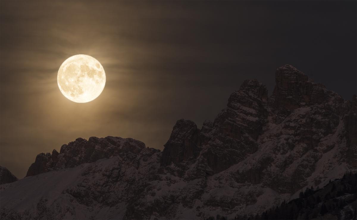 Photograph of the bright moon above silhouetted mountains. 