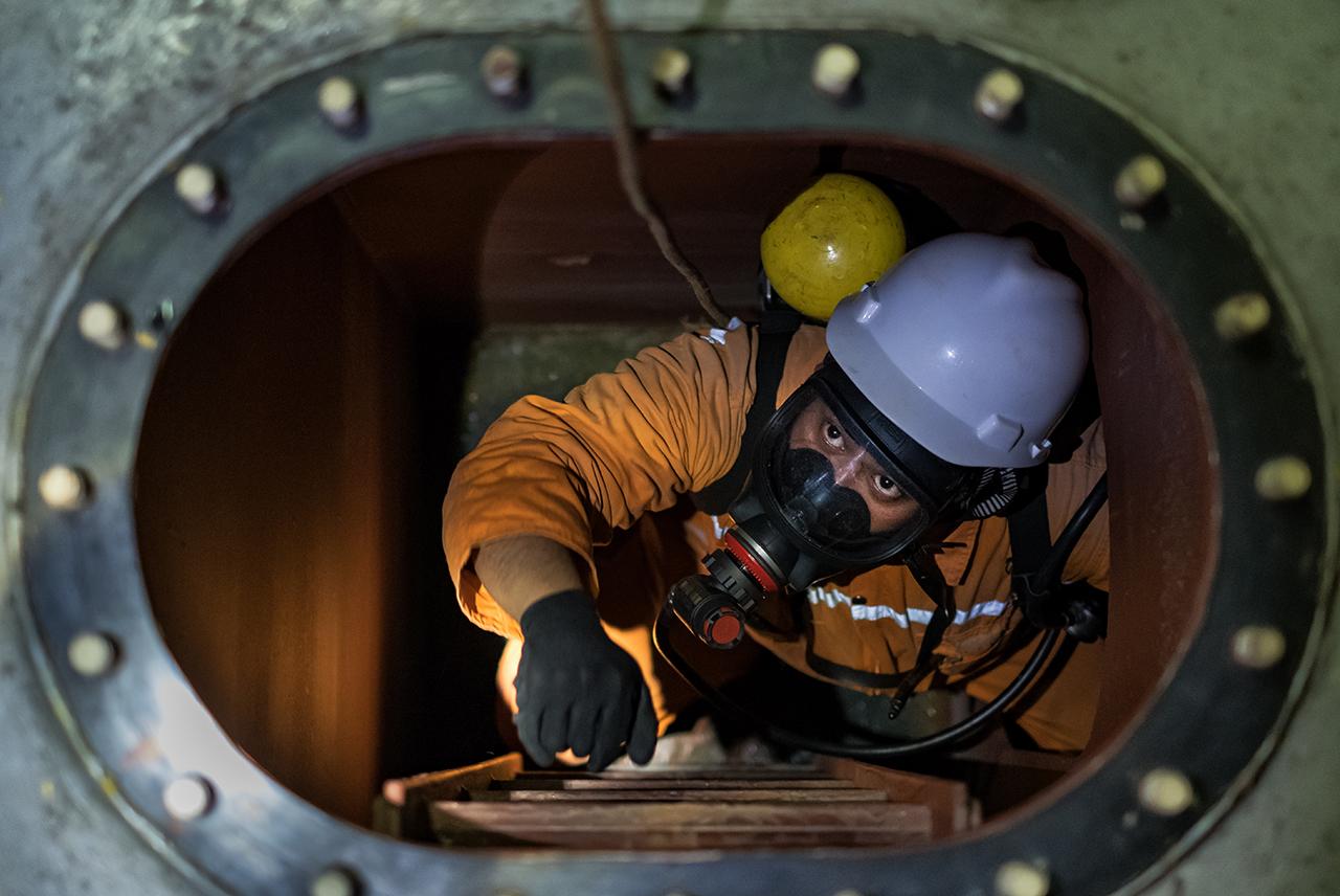 Photo looking down a narrow opening at a person on a ladder