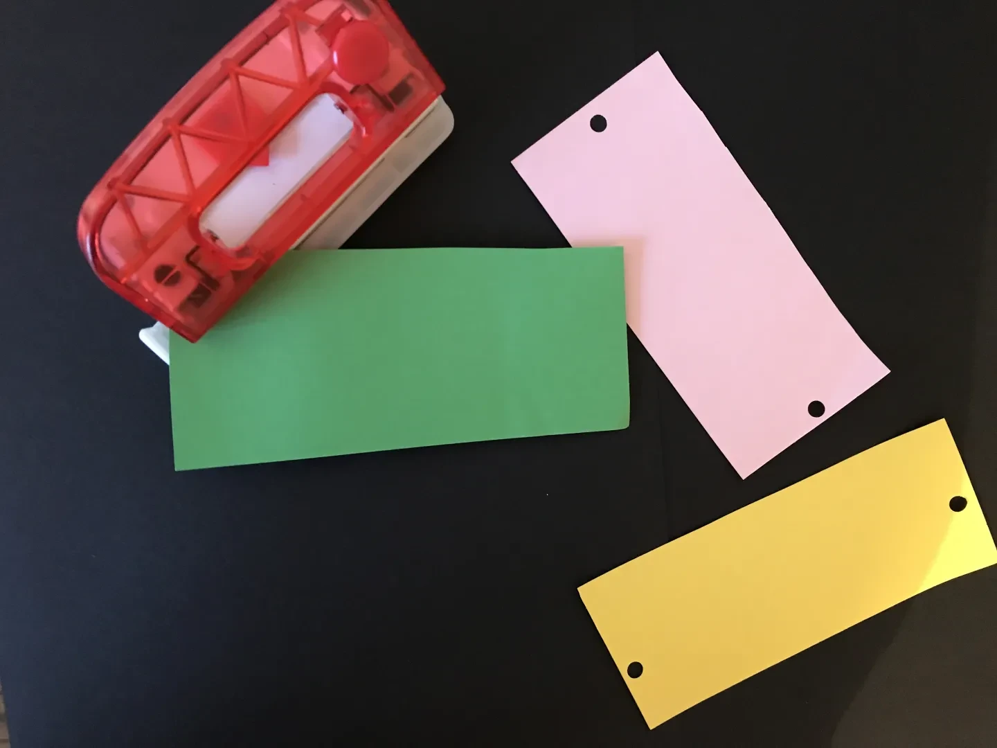 Three strips of coloured pieces of paper. Two have small holes at either end.
