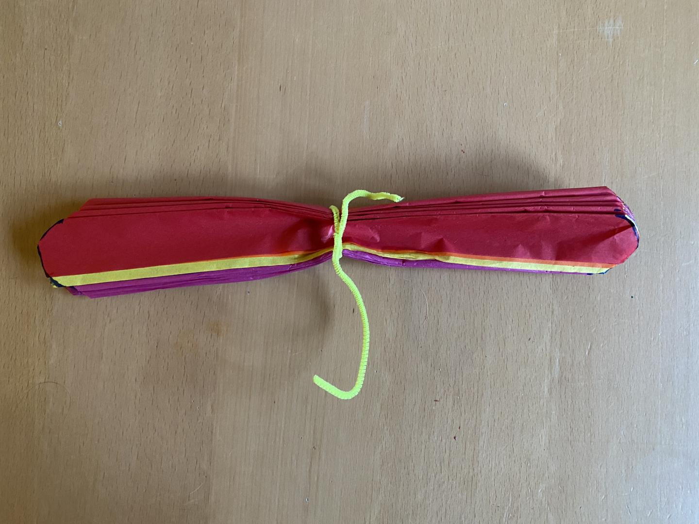 Stack of coloured tissue concertina folded papers with pipe cleaner tied around the middle