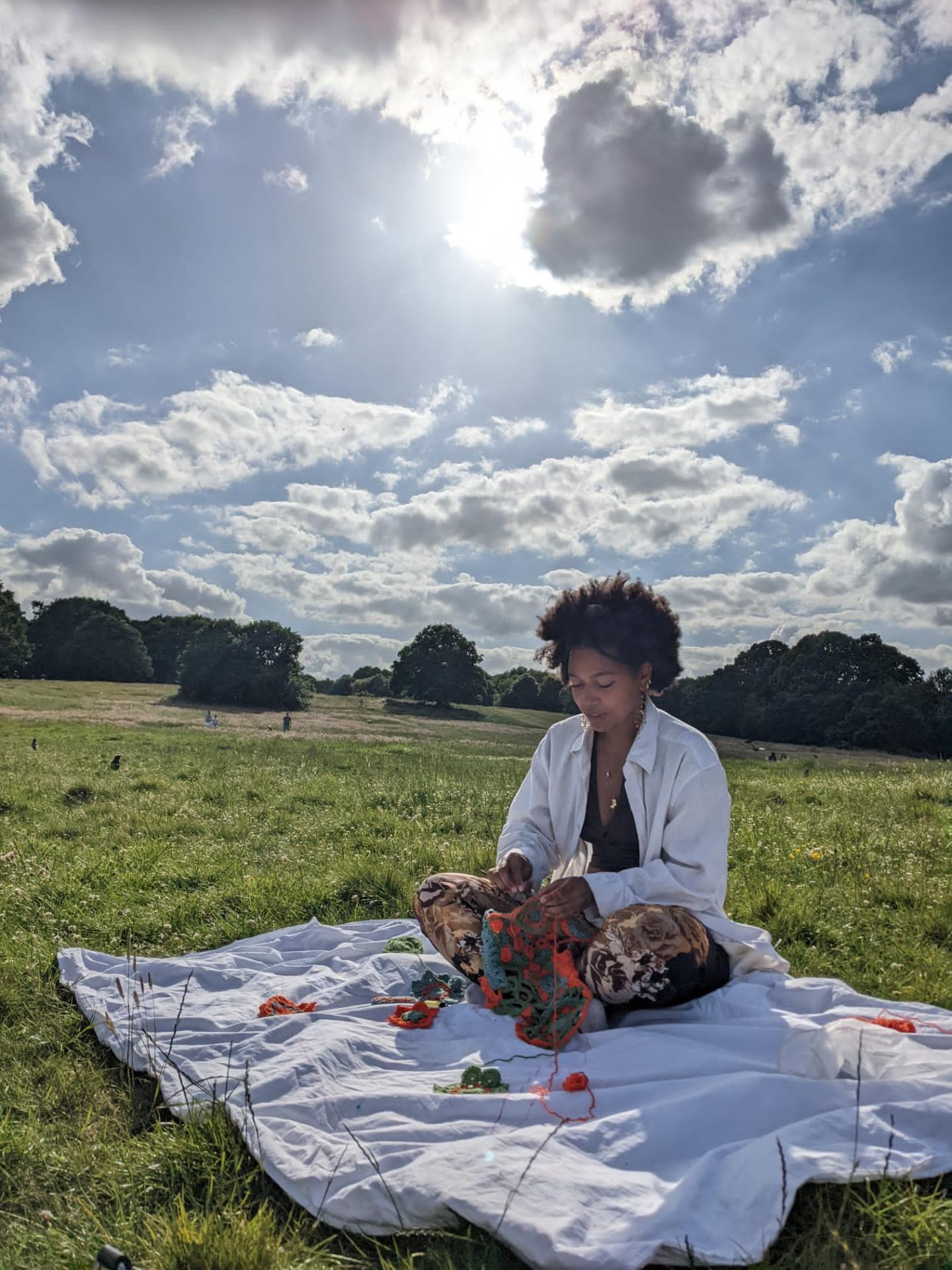 Photo of artist, Sarah Hawke, sitting on a blanket in field crocheting the Kanga. 