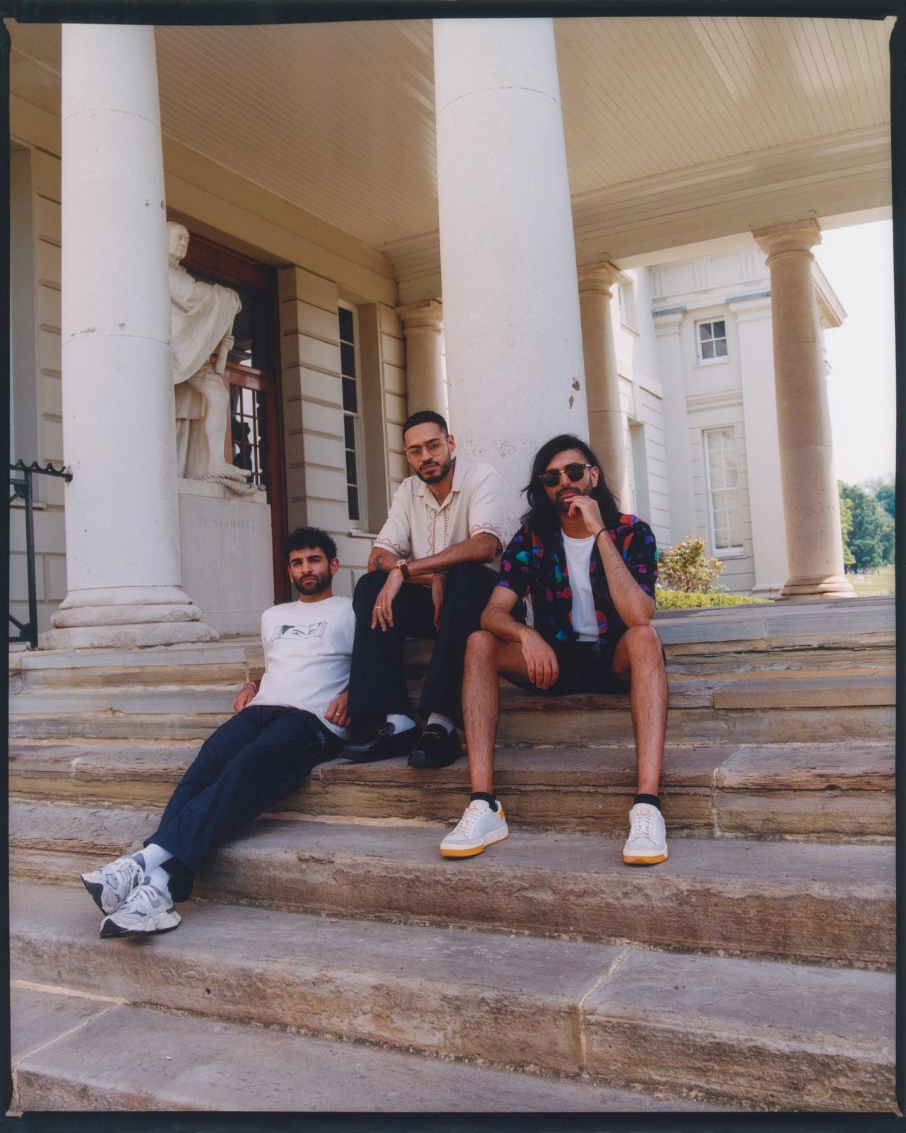 Group of three young Asian men sitting relaxed on steps outside a grand pillared building