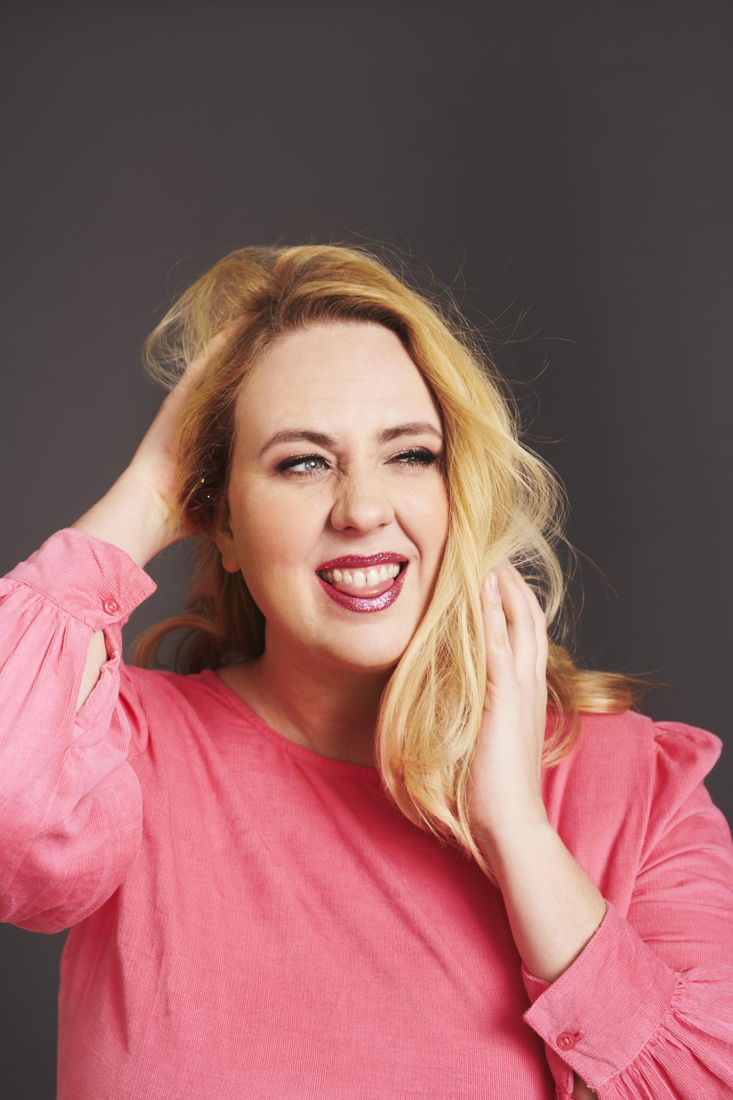Image of Helen Bauer, comedian, who has mid-length blonde hair and is wearing a pink jumper