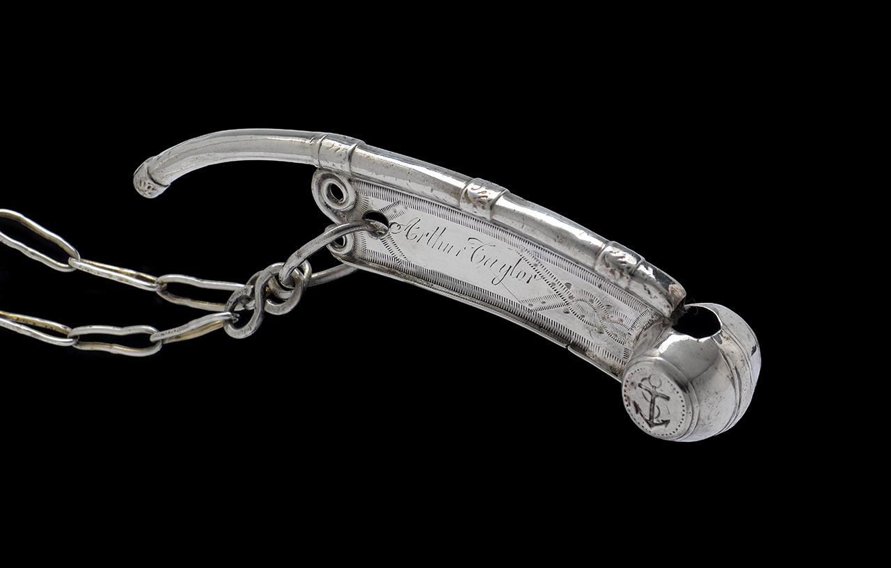 Image showing a silver boatswain's call, which is a long, thin whistle with a small barrel shape on the front