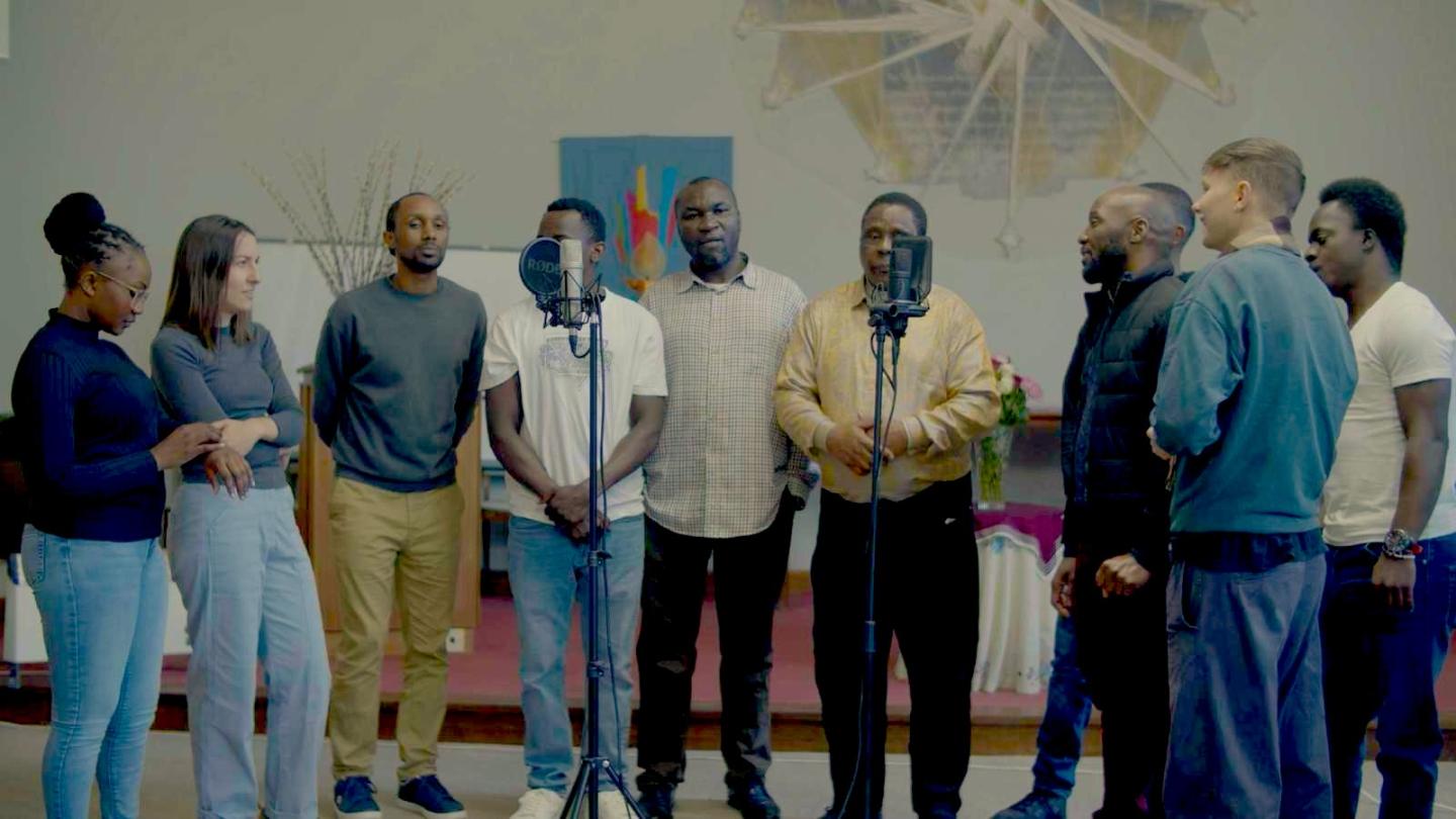 Photo of a group of people, standing and singing to microphones