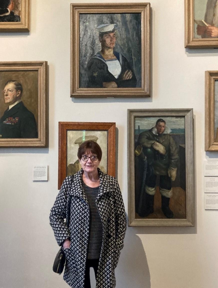 A woman poses below the portrait of the seaman that she is related to