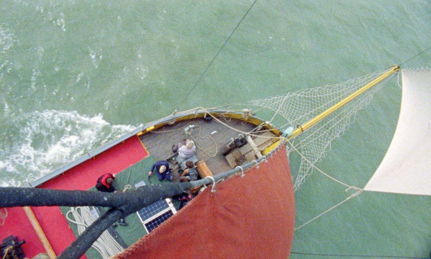 A view of Thames sailing barge Blue Mermaid looking down at the deck from the top of a mast, at people working below.