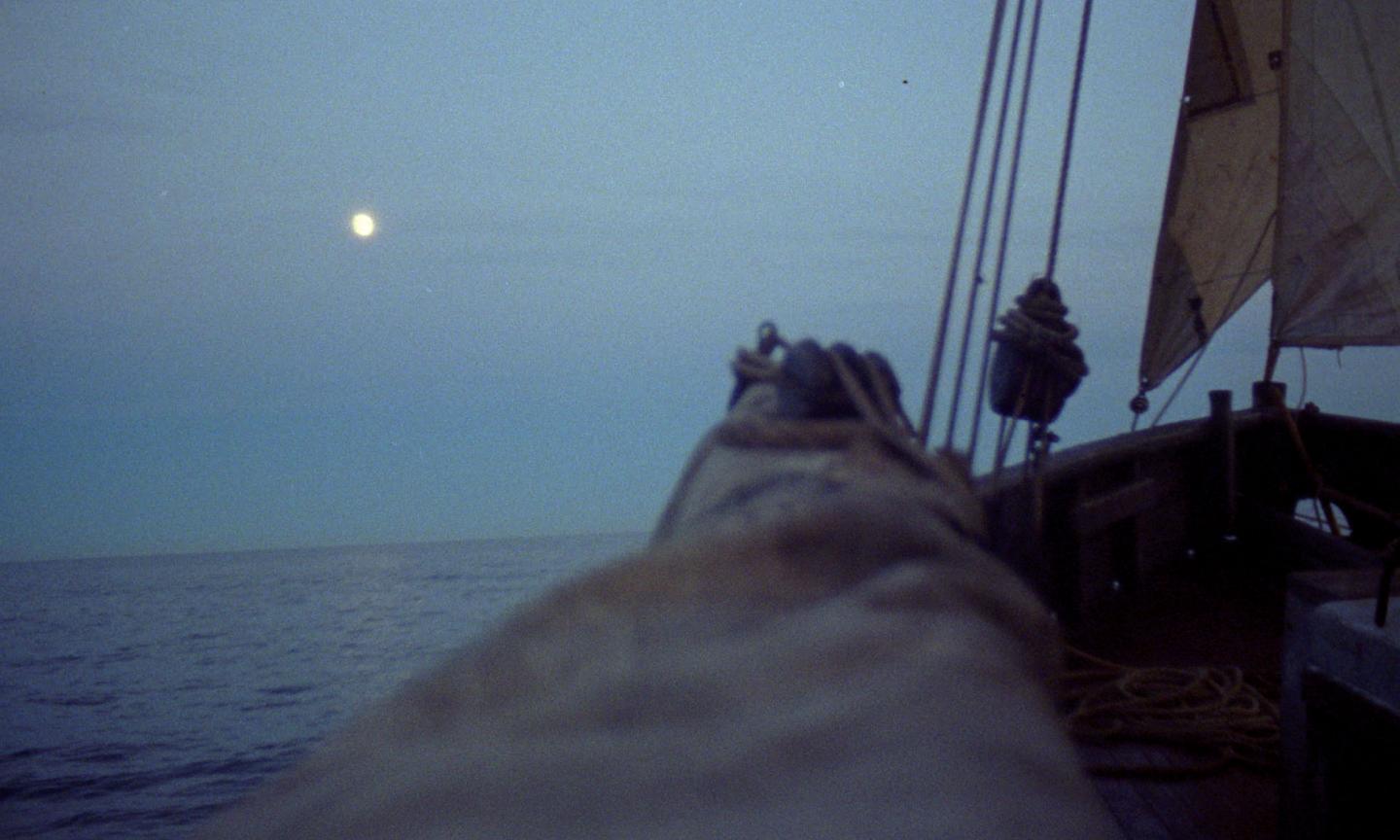The sky and sea are a dark blue colour with the moon in the background. To the right of the image is a partial view of a sailing vessel and rigging.